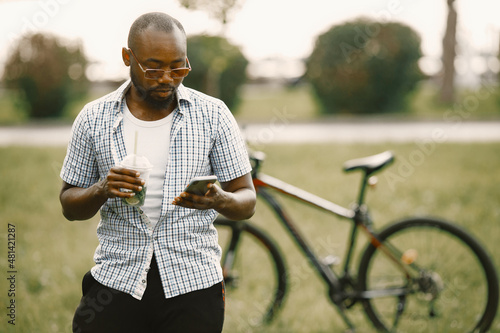 Black american man in a sunglasses standing on a grass and using a phone