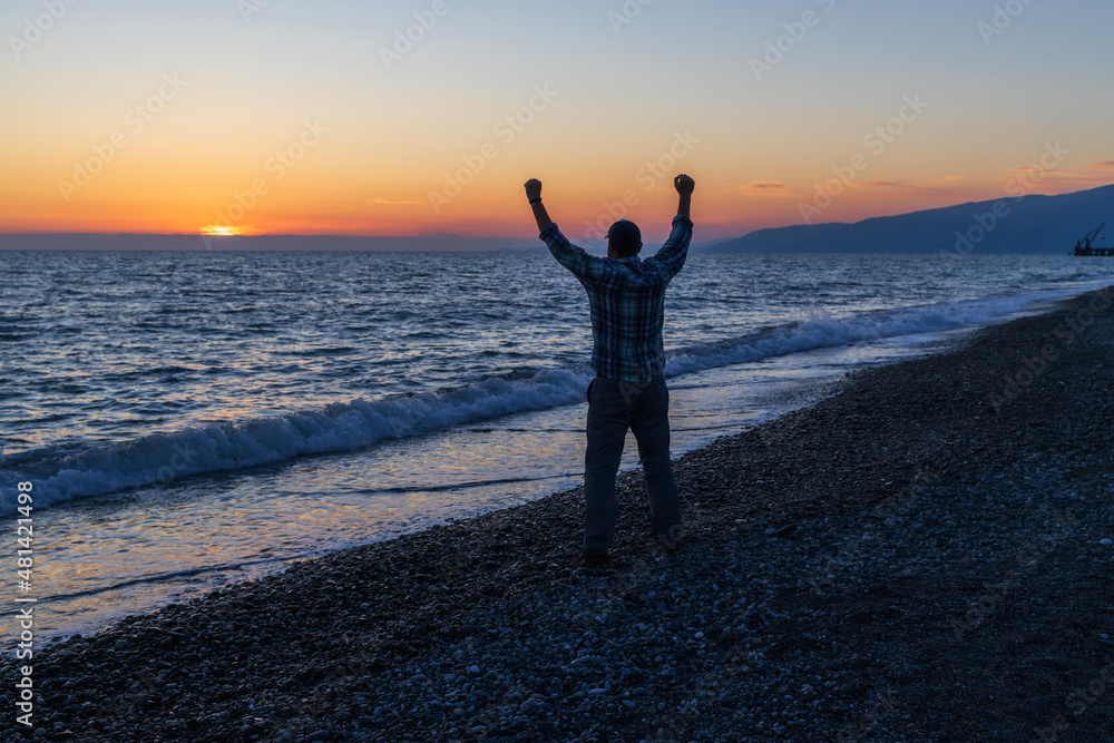 Fototapeta premium silhouette of a man who rejoices in the sea on the seashore in the evening