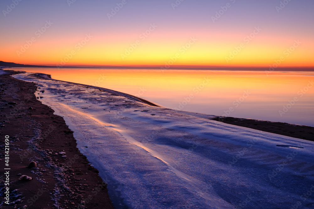 colorful beautiful sunset at sea in winter with snow on the beach