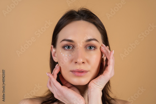 Close-up beauty portrait of a topless woman with perfect skin and natural make-up, with anti-aging cream dots to moisturize and firm the skin under the eyes.