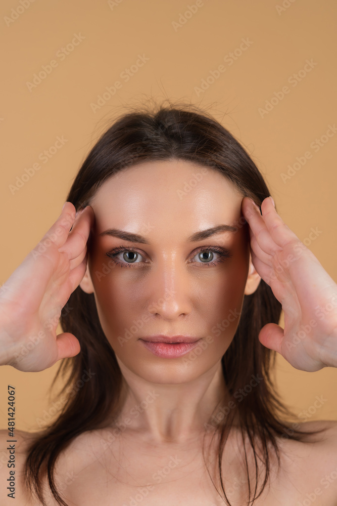Fototapeta premium Close beauty portrait of a topless woman with perfect skin and natural makeup, shiny lips, on a beige background