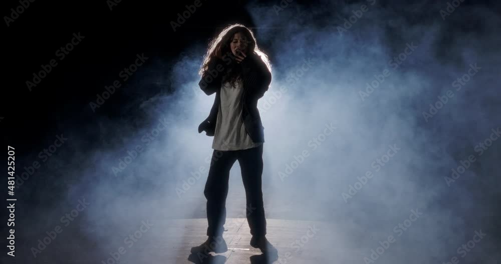 Young female dancer performing wild hip hop dance with strobe light and smoke background Young female dancer performing wild hip hop dance with strobe light and smoke background