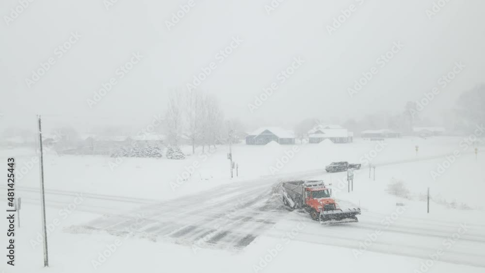 Drone view following the sand filled snow plow down a rural highway in a snowstorm. Gray snow filled sky. Obscured landscape. Drone view following the sand filled snow plow down a rural highway in a snowstorm. Gray snow filled sky. Obscured landscape.