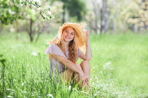 Attractive young blond woman outdoor. Closeup portrait of beautiful lady sitting on the grass