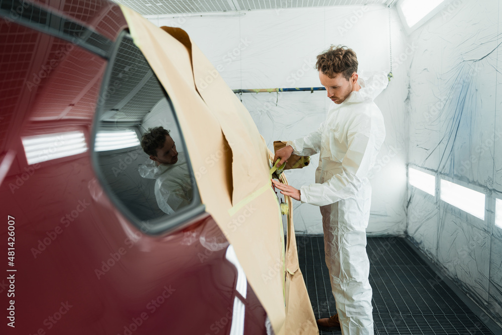 Male mechanic covering body car with paper and masking tape before painting in auto repair service. Preparing a car before spray paint Male mechanic covering body car with paper and masking tape before painting in auto repair service. Preparing a car before spray paint