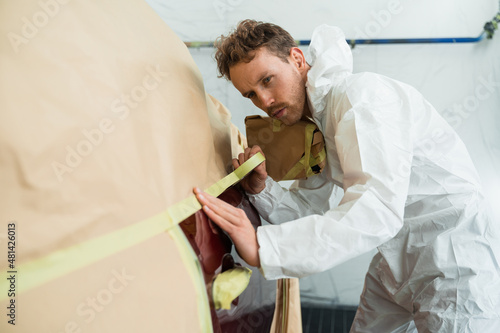 Fotografi Mechanic covering car body with paper and masking tape before painting in auto r