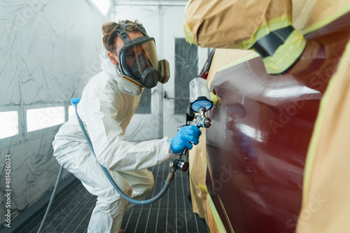 Foto Auto painter in a protective suit and mask sprays a degreaser or other cleaner on a car door using a spray gun