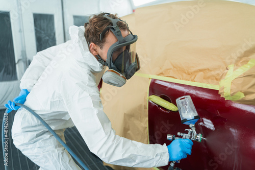 Auto painter in a protective suit and mask sprays a thinner or other cleaner on a car door using a spray gun. Preparation of vehicle body elements for local repair
