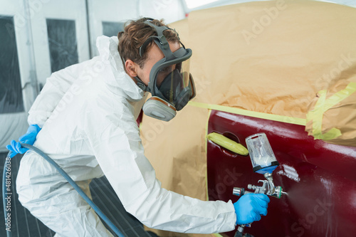 Auto painter in a protective suit and mask sprays a thinner or other cleaner on a car door using a spray gun. Preparation of vehicle body elements for local repair photo