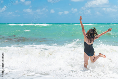 Fotografiet Back of young woman in swimsuit jumping running to green turquoise water in Sunn