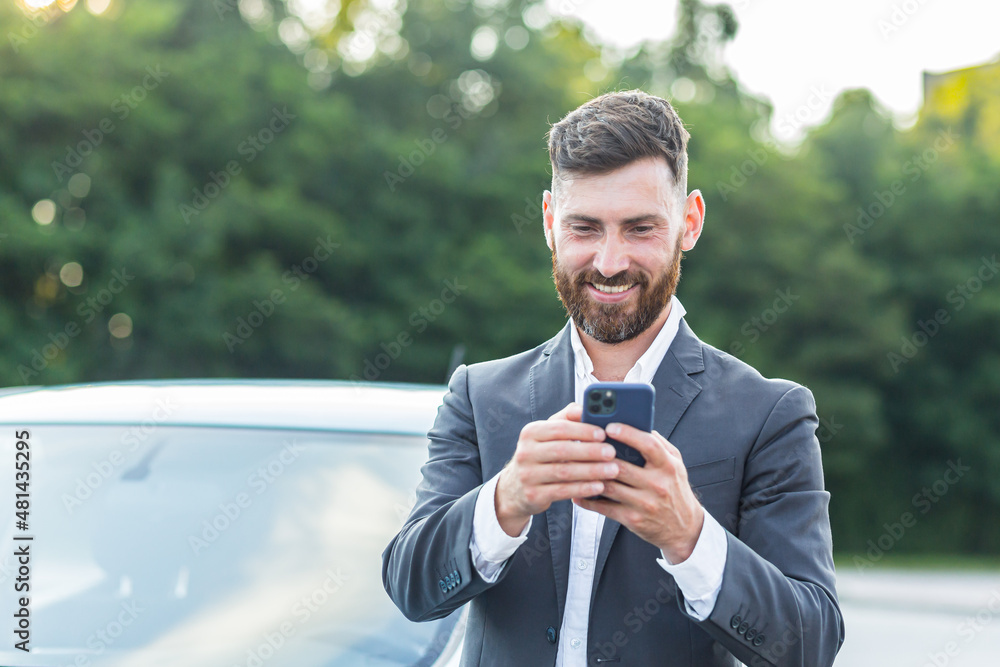 © Liubomir - Cheerful and successful male businessman car salesman uses the phone near the parking lot to sell cars