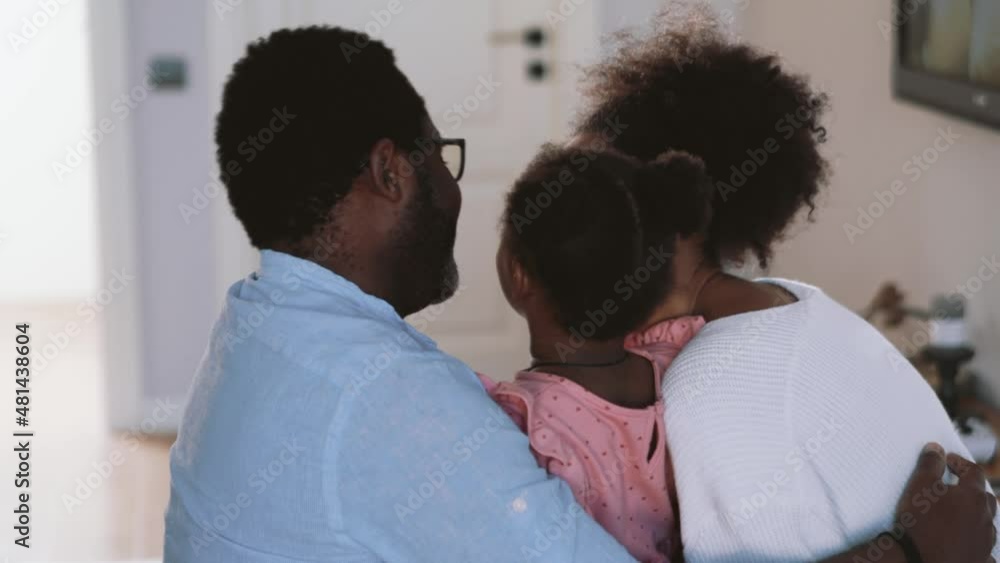 Positive little African girl running and hugging her parents at home Positive little African girl running and hugging her parents at home