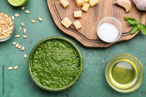 Bowl of tasty pesto sauce and ingredients on green background