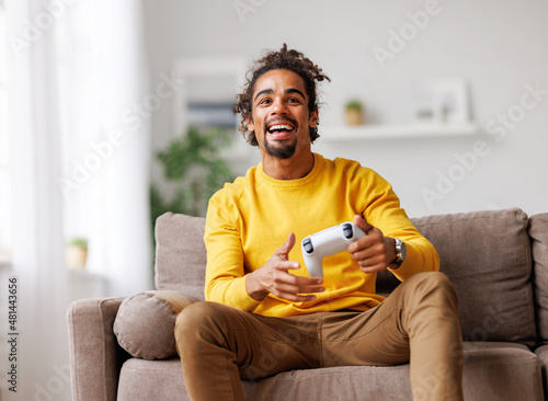 Young positive happy african american guy with wireless gamepad playing video game at home photo