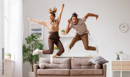 Young energetic active african american family couple jumping on sofa, having fun together at home photo