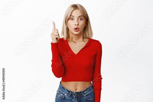 Eureka. Surprised young woman has an idea, pointing fige rup, showing top promo, expressing her thougts and plans, standing over white background photo