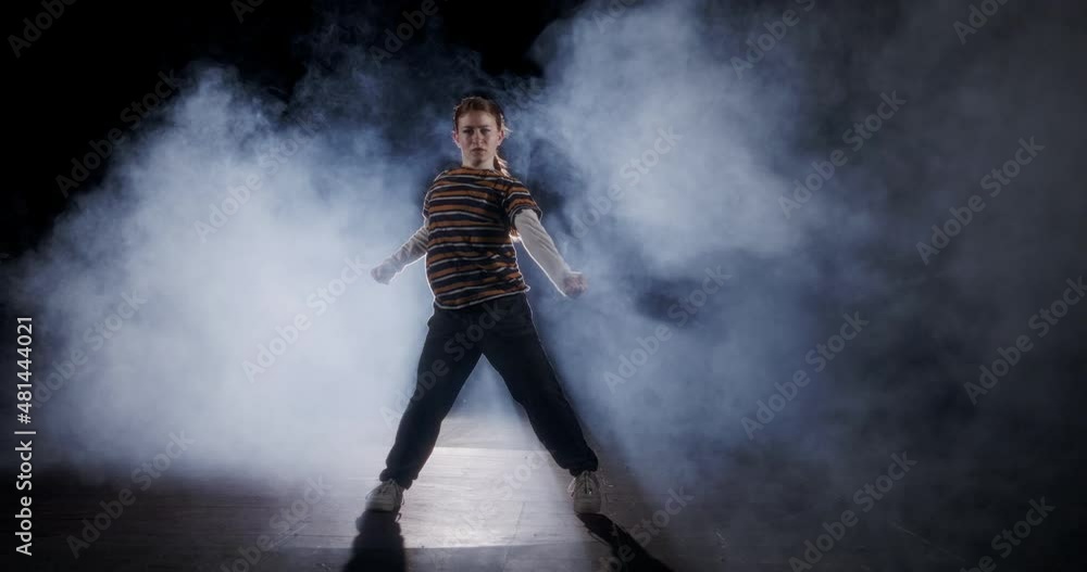 Teenage female dancer performing hip hop dance in slow motion with strobe light and smoke background Teenage female dancer performing hip hop dance in slow motion with strobe light and smoke background