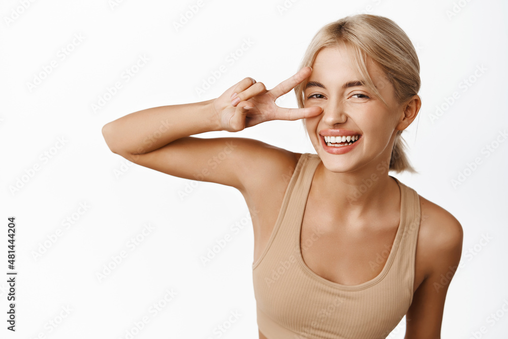 Close up portrait of healthy and fit fitness instructor, female athlete showing peace sign and looking happy, inviting to gym, workout sport classes, white background Close up portrait of healthy and fit fitness instructor, female athlete showing peace sign and looking happy, inviting to gym, workout sport classes, white background