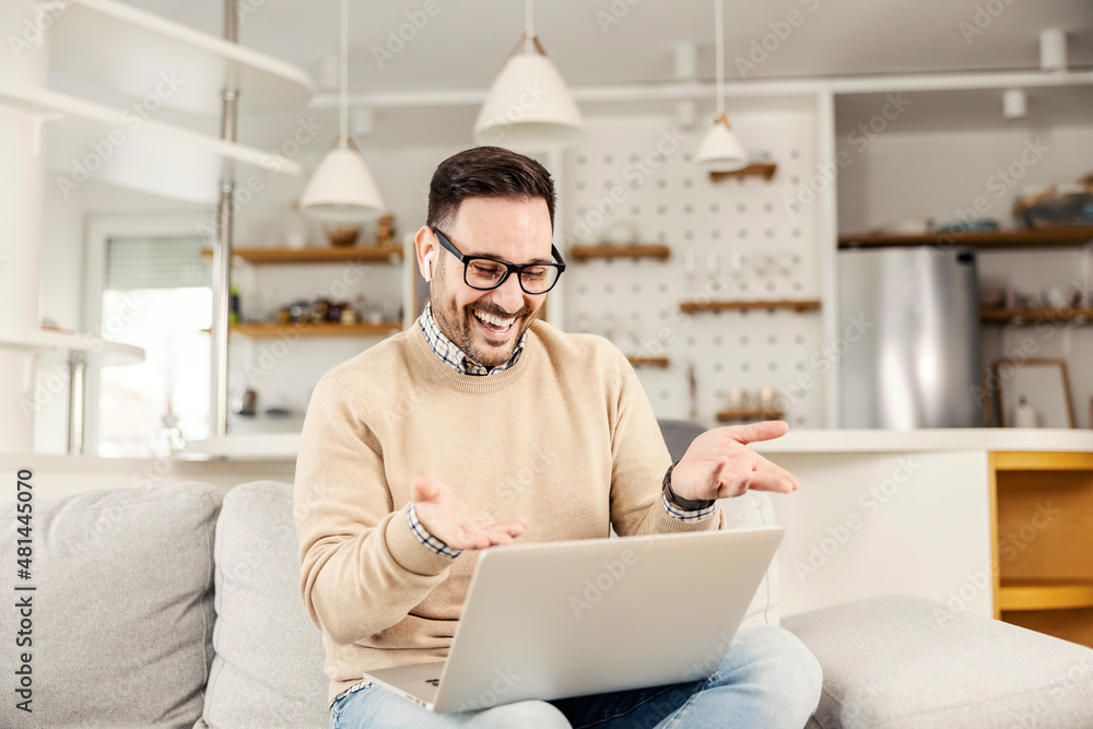 A happy man sitting at his cozy home and having video call on the laptop. A man is laughing and looking at the laptop. A happy man sitting at his cozy home and having video call on the laptop. A man is laughing and looking at the laptop.