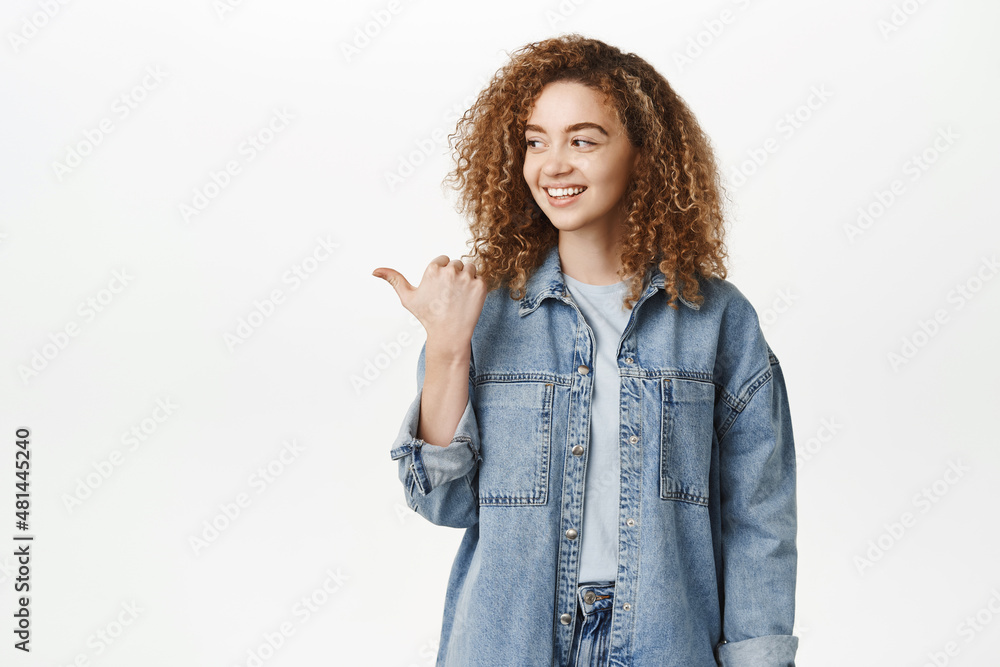 Portrait of young curly woman pointing left and smiling cheerful, showing advertisement, standing in casual clothes over white background Portrait of young curly woman pointing left and smiling cheerful, showing advertisement, standing in casual clothes over white background