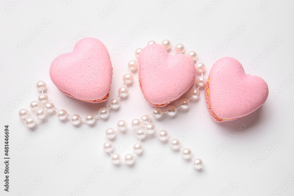Tasty heart-shaped macaroons and beads on white background