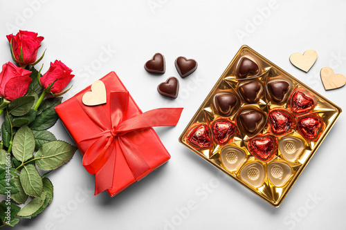Composition with tasty heart-shaped candies and flowers on white background