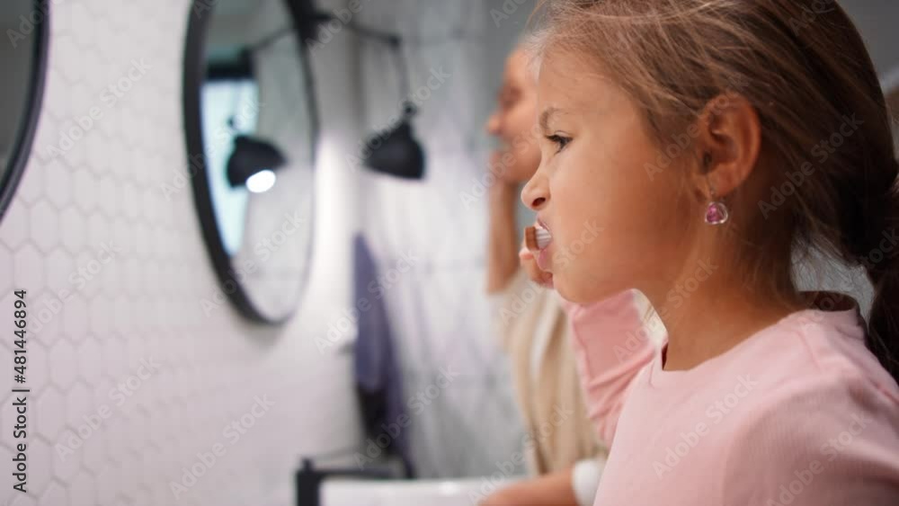 Little girl brushing teeth in bathroom at home in morning, together with her senior grandmother. Little girl brushing teeth in bathroom at home in morning, together with her senior grandmother.