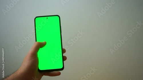 Man using smartphone viewing green screen scrolling on mobile phone browsing chroma key . close up male hands . Mobile phone mock-up