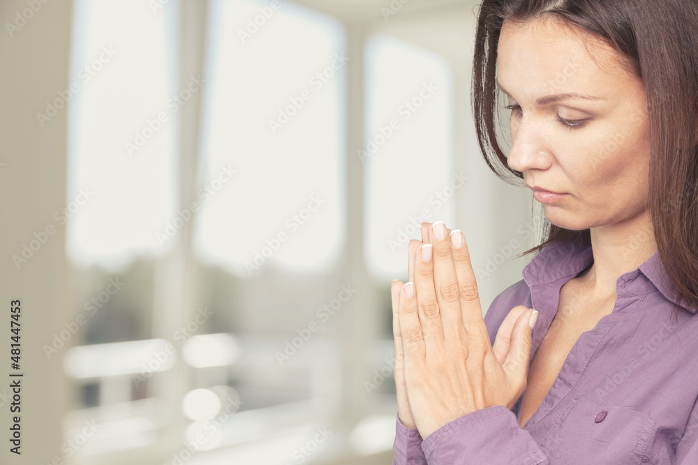 Religious young woman with clasped hands praying indoors at home Religious young woman with clasped hands praying indoors at home