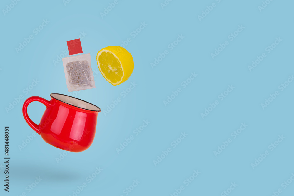 Obraz premium Creative concept made of red tea cup with flying tea bag and lemon slice on a blue background.