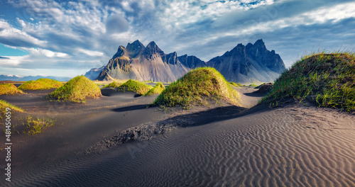 Dramatic afternoon view of Stokksnes cape with Vestrahorn (Batman Mountain) on background. Amazing summer landscape of black sand dunes with green grasson the top. Travel to Iceland.