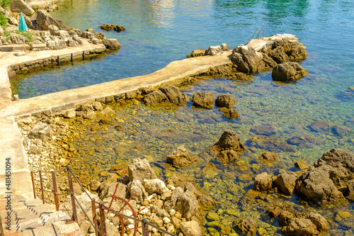 Rocky pier with stairs to enter the sea with transparent blue water of Adriatic Sea for swimming in Croatia.