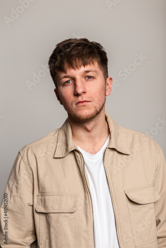 Fashion young man with stylish hairstyle in beige jacket and t-shirt on a gray background in the studio. Handsome guy look at the camera