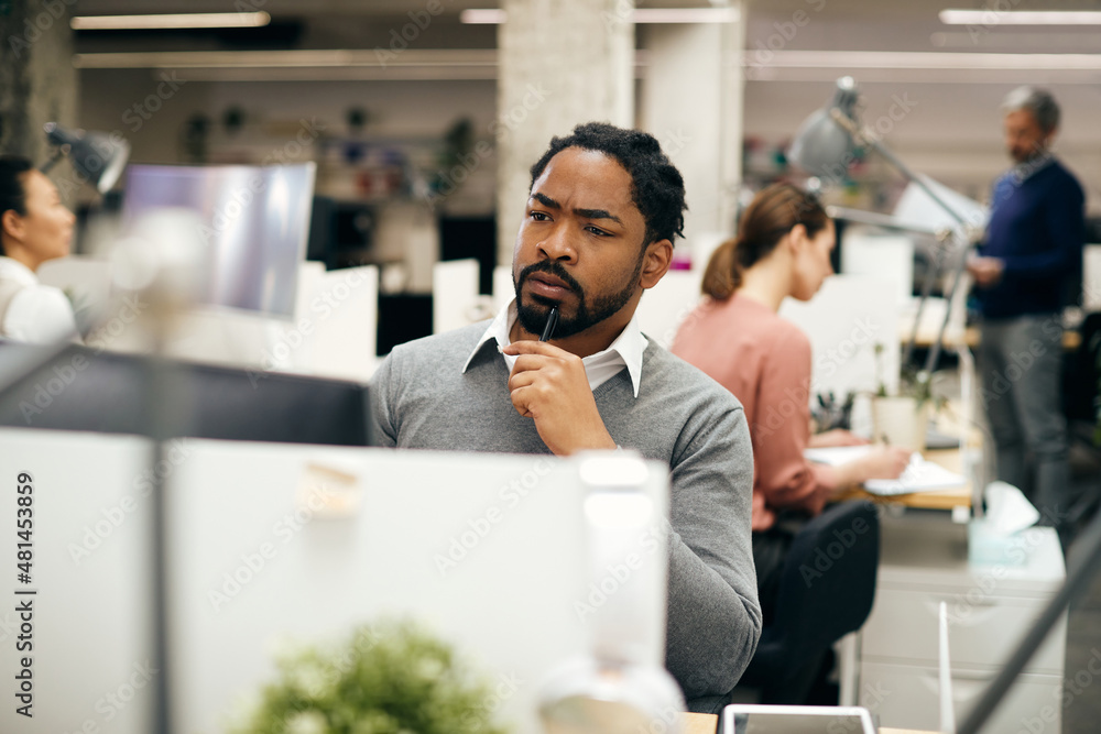 Pensive black businessman reads problematic e-mail on computer while working at corporate office. Pensive black businessman reads problematic e-mail on computer while working at corporate office.