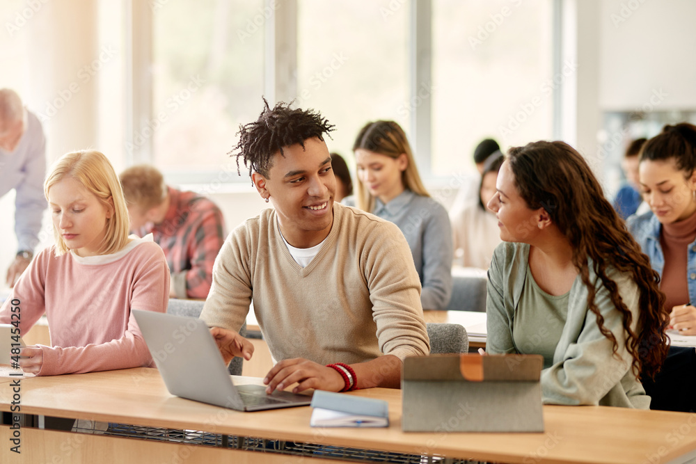 Happy African American student and his Caucasian classmate talk while learning on laptop at university classroom. Happy African American student and his Caucasian classmate talk while learning on laptop at university classroom.
