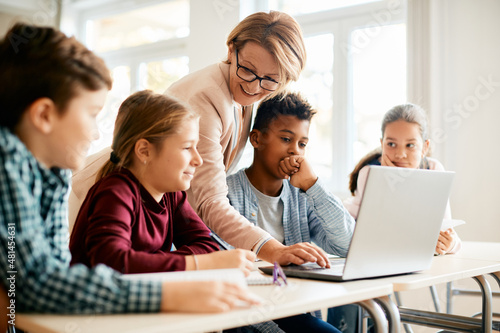 Happy teacher and her students use laptop during computer class at elementary school.