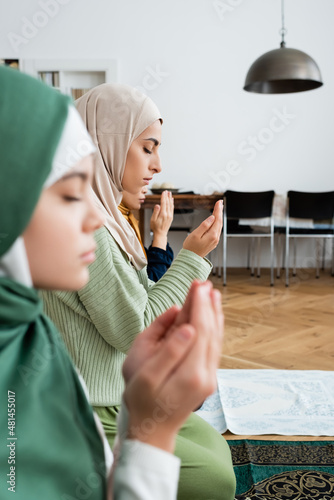 Side view of arabian woman in traditional clothes praying near family at home.