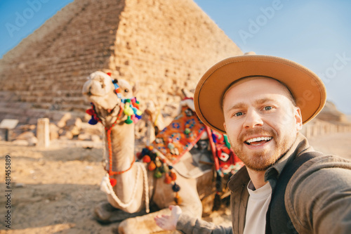 Travel selfie photo tourist man in hat with camel background pyramid of Egyptian Giza, sunset Cairo, Egypt
