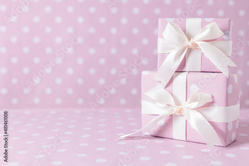 Gift boxes tied with satin ribbons stand on a pink background.