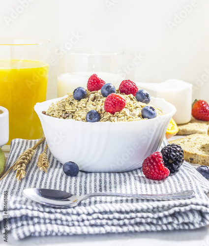 healthy breakfast of granola with blueberries and raspberries in a white porcelain bowl, with fruit, milk, coffee and wheat toast. front view photo