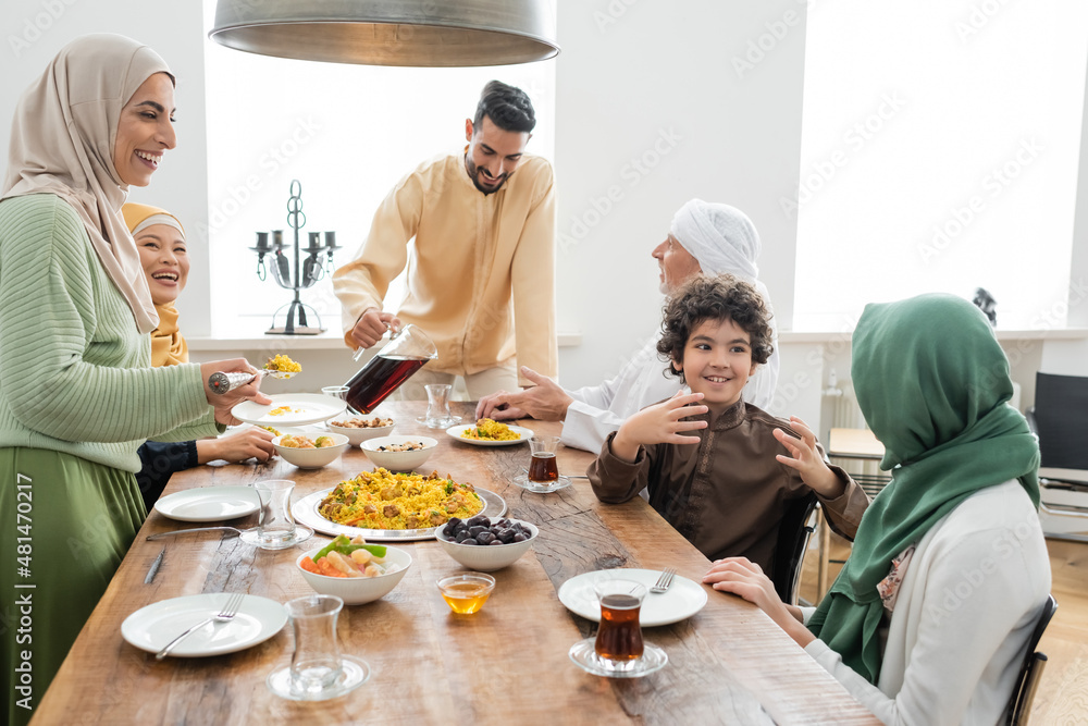 Cheerful interracial family serving pilaf and pouring tea near dinner at home. Cheerful interracial family serving pilaf and pouring tea near dinner at home.