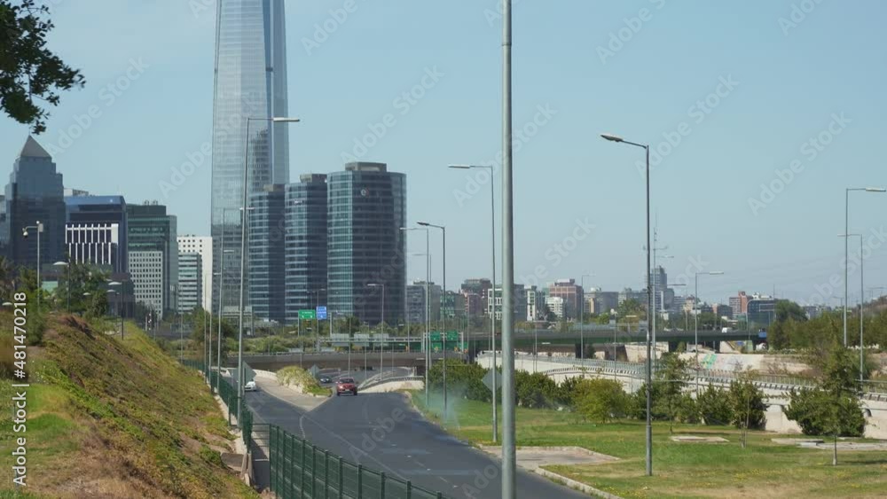 Jib down of cars driving near Bicentenario Park and modern skyline in background at daytime, Santiago, Chile Jib down of cars driving near Bicentenario Park and modern skyline in background at daytime, Santiago, Chile