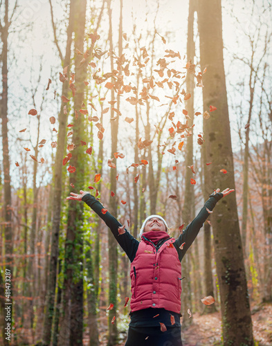 a woman opens her arms under dry leaves flying through the air at sunset in a forest. she is happy. nature and environment concept. care of forests.