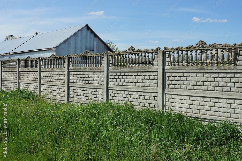 long gray concrete fence wall on a rural street in green grass against the sky