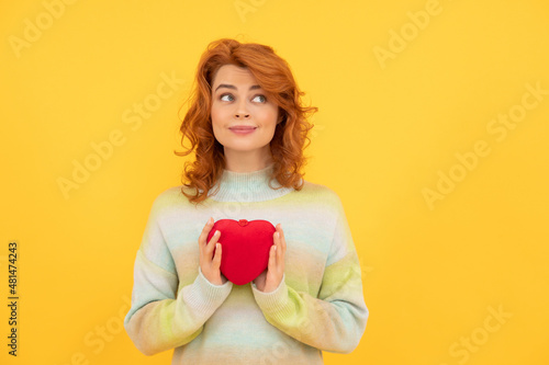 pondering cheerful redhead woman with red heart on yellow background. valentines