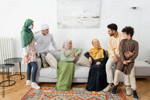 Canvas Print happy interracial women sitting on sofa near muslim family at home
