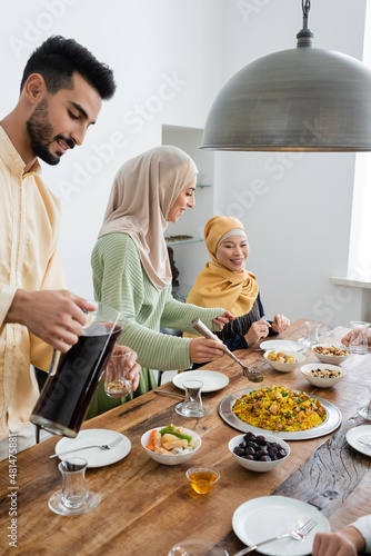 Smiling arabian woman standing near food, husband with tea and asian mom at home.