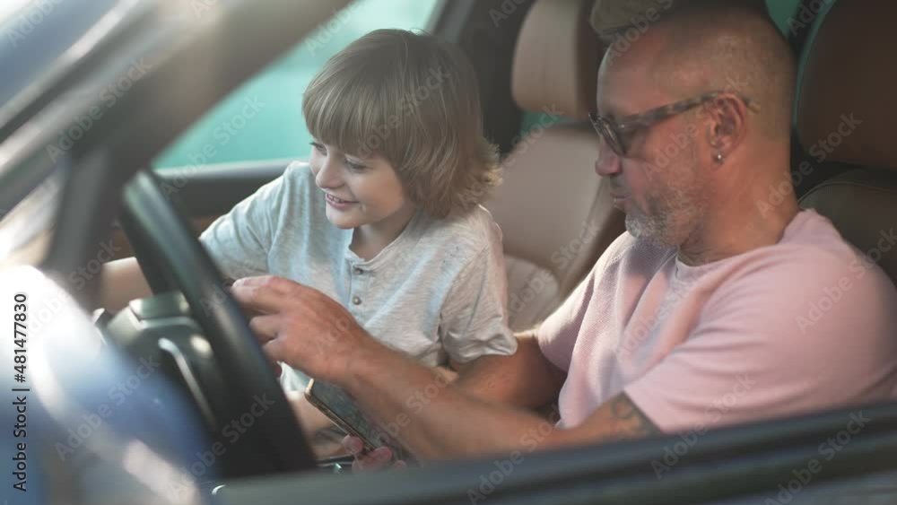 Happy Caucasian boy sitting in car with man talking surfing Internet on smartphone. Portrait of excited son with confident father in new automobile outdoors on sunny day. Family and success concept Happy Caucasian boy sitting in car with man talking surfing Internet on smartphone. Portrait of excited son with confident father in new automobile outdoors on sunny day. Family and success concept