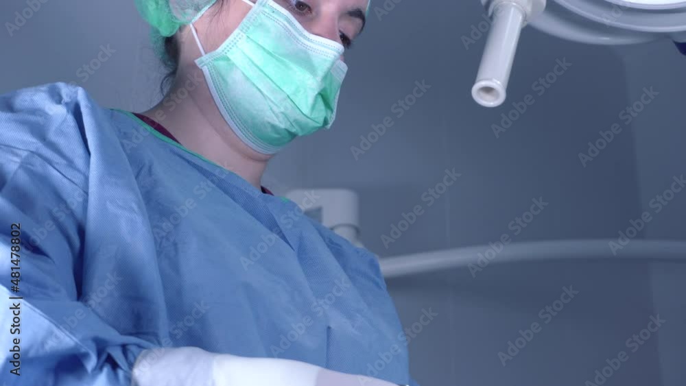 Tilt up shot of Female surgeons in medical uniform using professional tools while standing under bright light in operating theater. High quality 4k footage Tilt up shot of Female surgeons in medical uniform using professional tools while standing under bright light in operating theater. High quality 4k footage