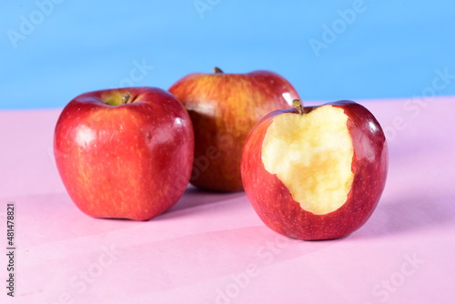 beautiful red apples seen from the side isolated on pink and blue background, bitten apple © Giovanni.Seabra